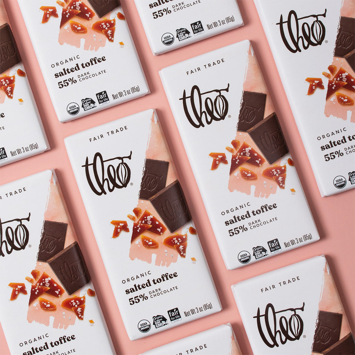Multiple Theo chocolate bars with salted toffee flavor packaging on a pink background