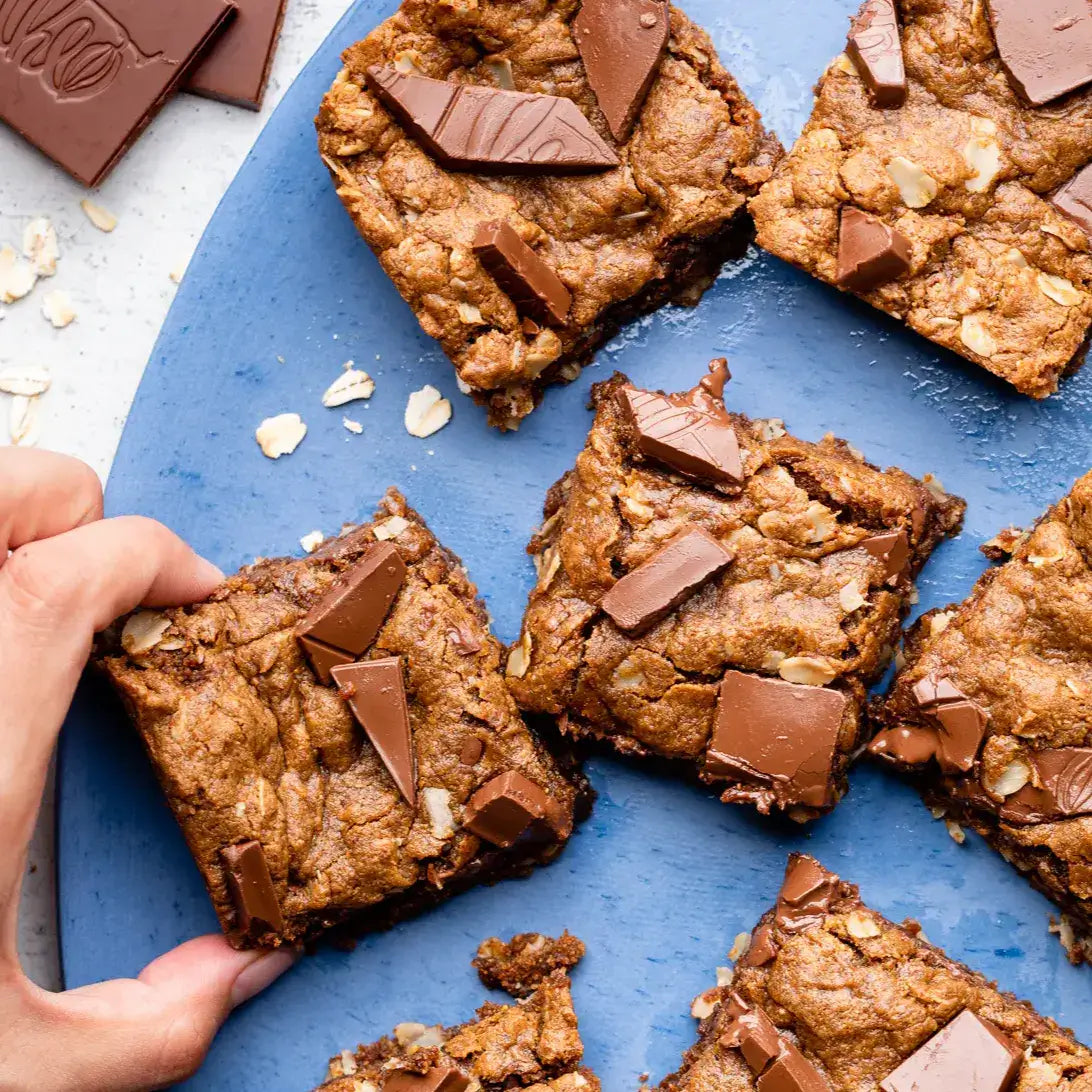 Chocolate oat bars on a blue plate with a hand reaching for one bar.